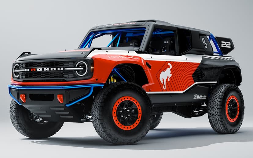 Orange and white Ford Bronco DR racing truck with blue roll cage and beadlock wheels on a white background.