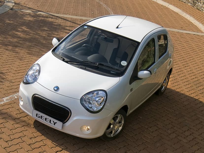White Geely Panda hatchback parked on a reddish-brown brick pavement under bright outdoor sunlight.