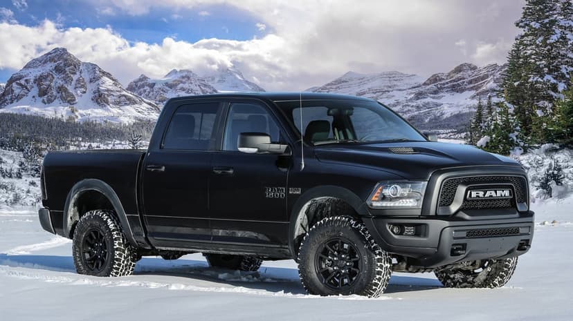 Black Ram 1500 truck parked in a snowy field with massive snow-capped mountains under a bright, cloudy blue sky.