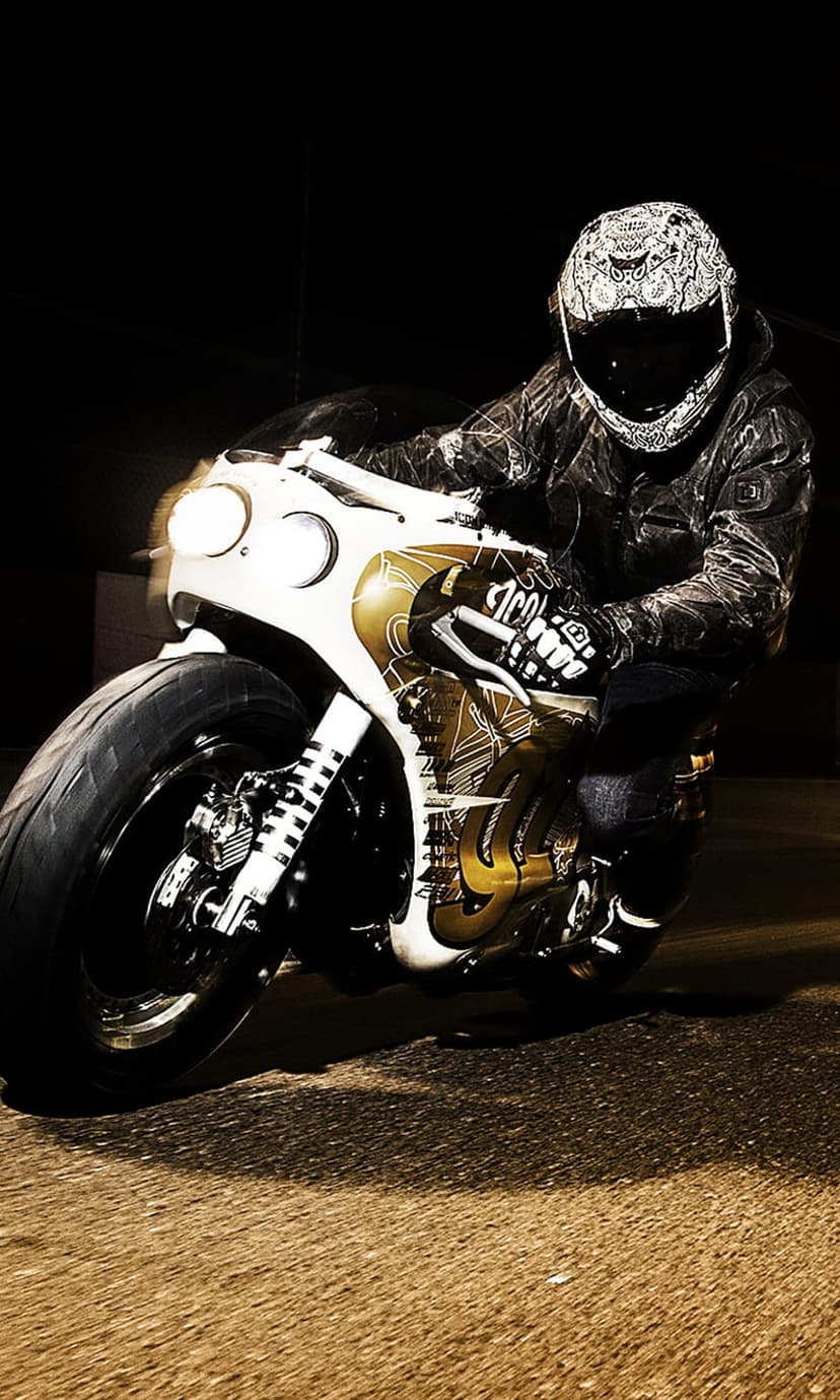 Motorcycle rider in a leather jacket and patterned helmet speeds on a custom bike through dark city streets.