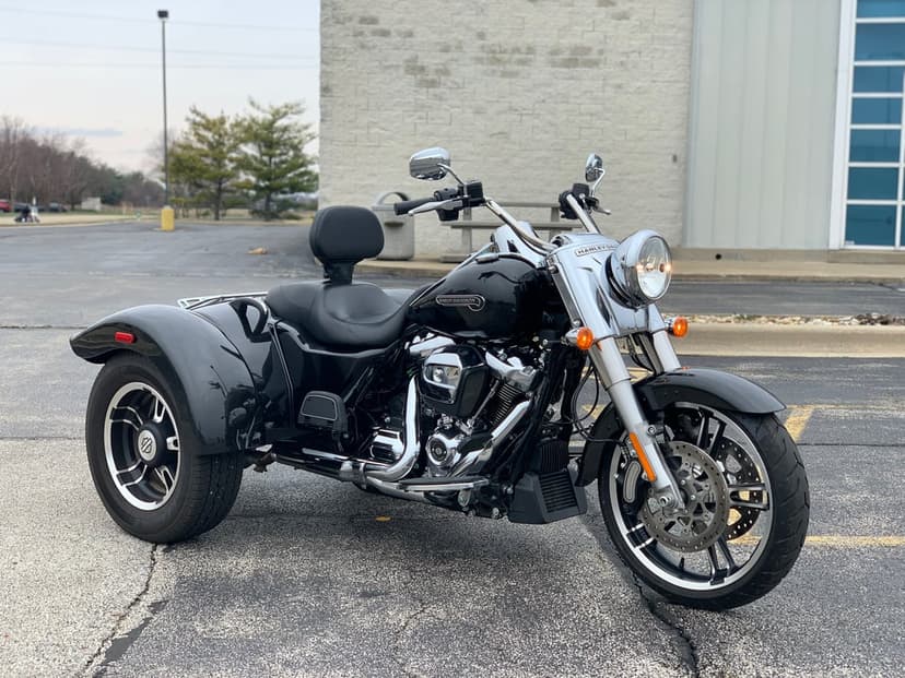 Black Harley-Davidson trike with chrome engine parked on asphalt against a neutral building background.