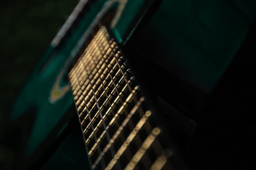 Guitar frets and strings shimmer with golden light reflections against a dark green blurred background.