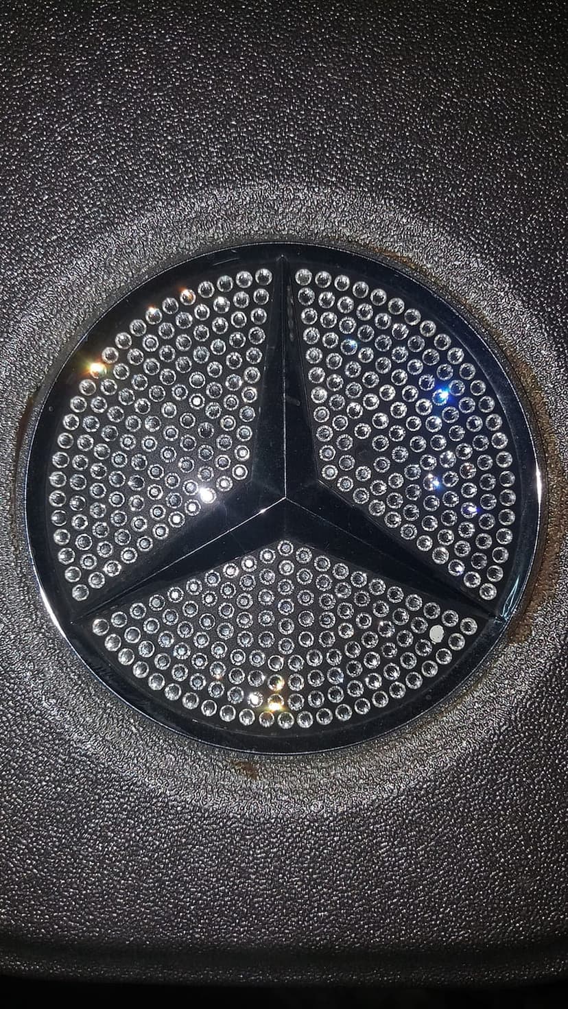 Mercedes-Benz star emblem encrusted with sparkling rhinestones set against a black textured interior surface.