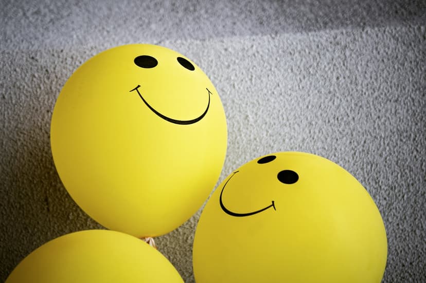 Three yellow smiley face balloons float together against a textured gray background with soft shadows and light.
