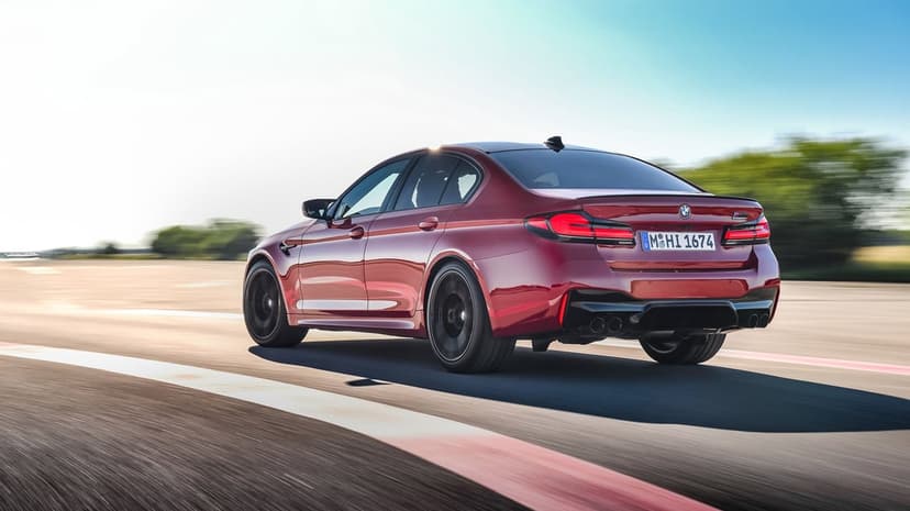 Red BMW M5 Competition racing on an asphalt track with motion blur under a bright, clear blue sky.