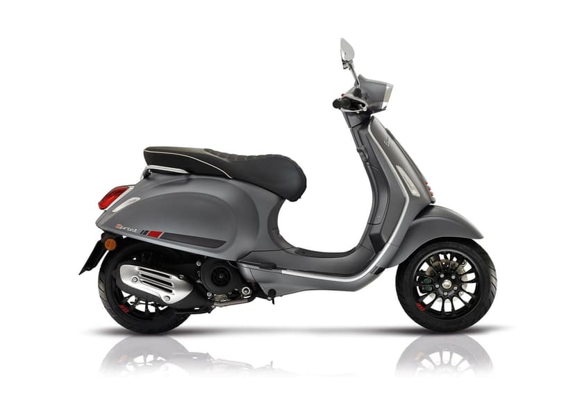 Profile view of a matte grey Vespa Sprint scooter with black wheels and red accents against a white backdrop.