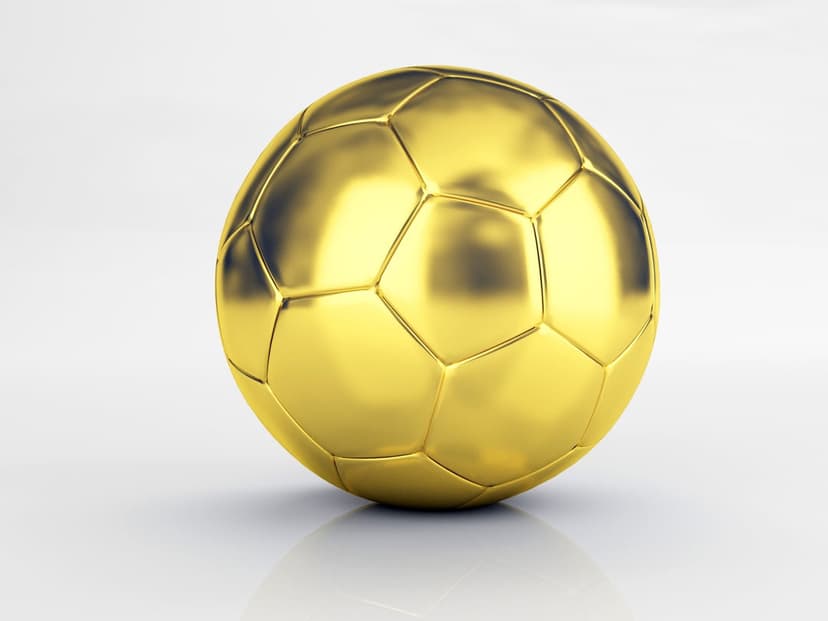 Golden soccer ball trophy with reflective metallic panels sits on a white surface with subtle lighting.