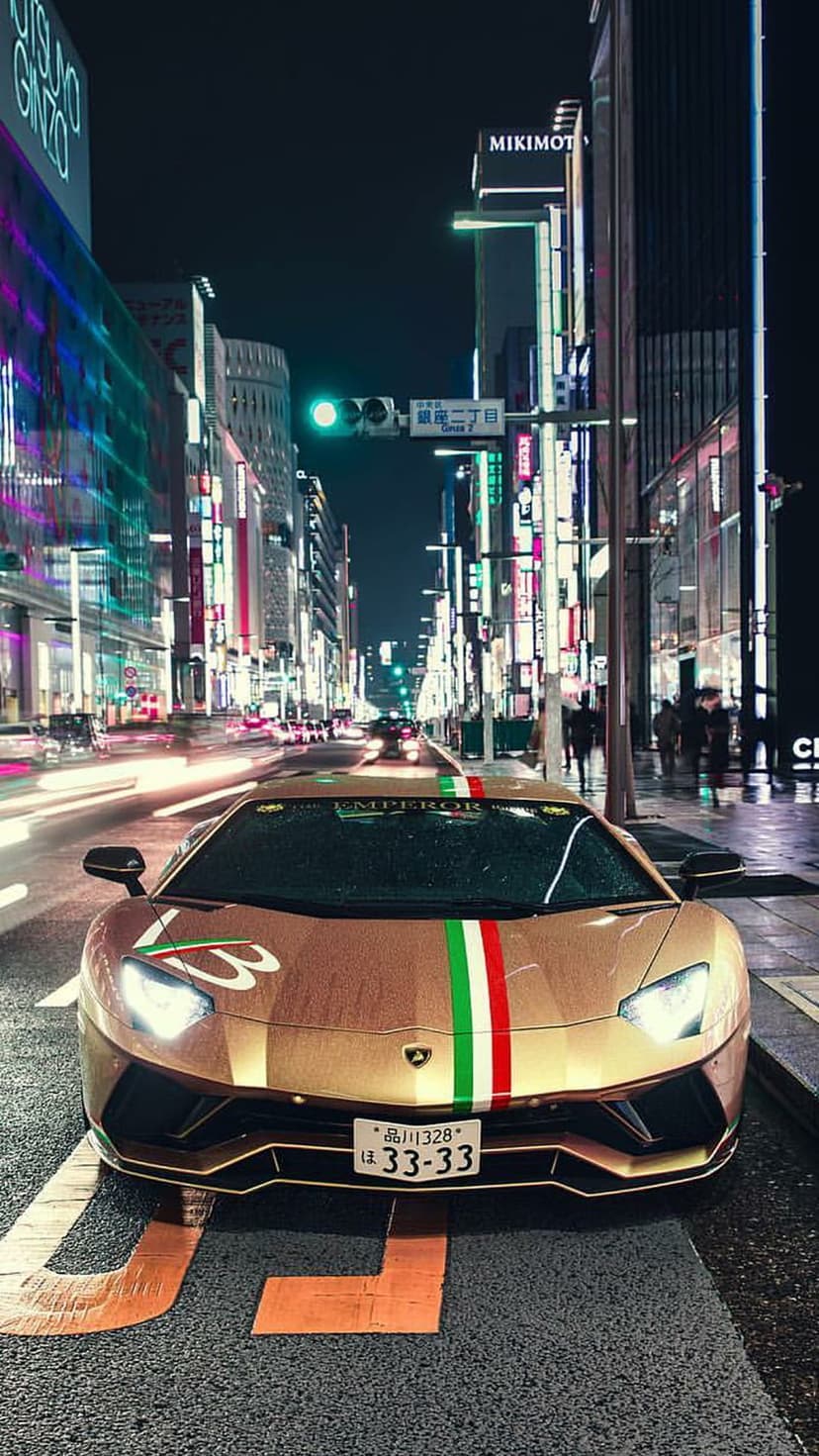 Gold Lamborghini with Italian racing stripes parked on a wet street amidst glowing Tokyo neon city lights.