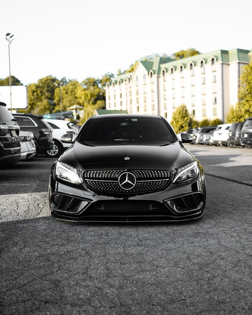 Black Mercedes C-Class sedan with a chrome grille parked on asphalt in front of a multi-story hotel building.