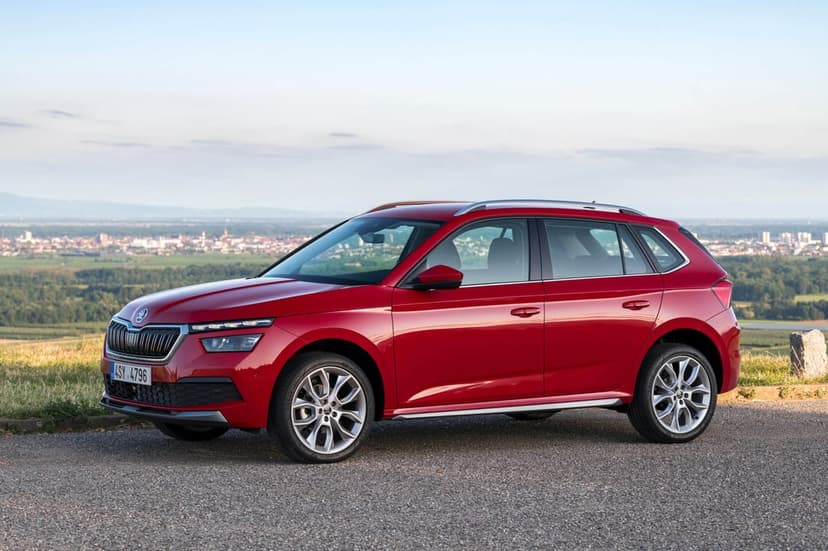Red SUV parked on an asphalt path overlooking a wide landscape of green fields and a distant town.