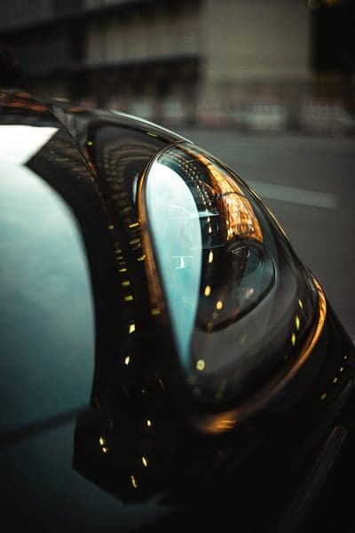 Close-up of a black car headlight with city lights reflection