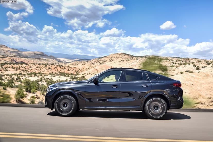 Black BMW X6 M driving on a desert road under a blue sky with canyon hills in the background.