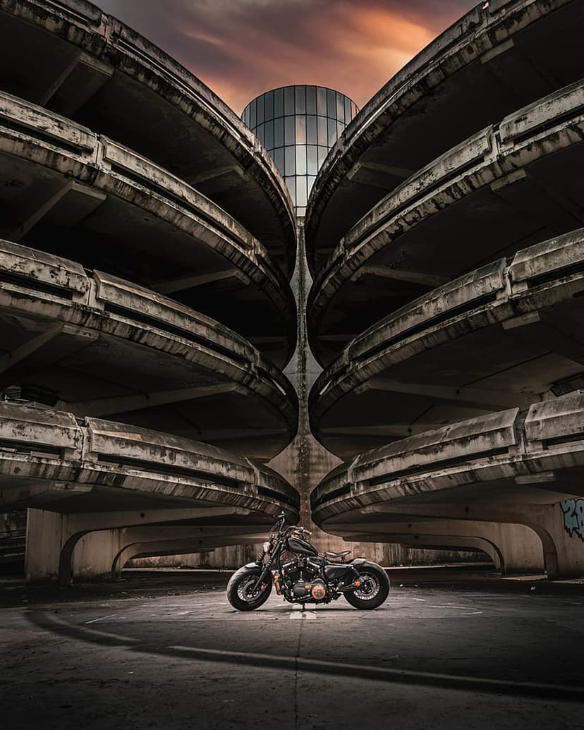 Custom black motorcycle parked between curved concrete pillars in a parking garage during a moody urban sunset.