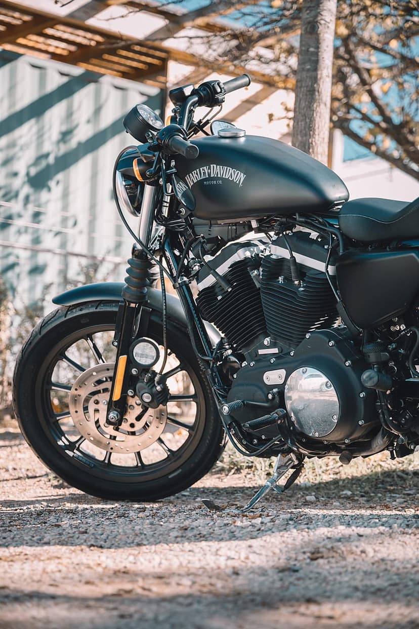 Matte black motorcycle engine and fuel tank with Harley-Davidson lettering parked on a textured gravel pathway.