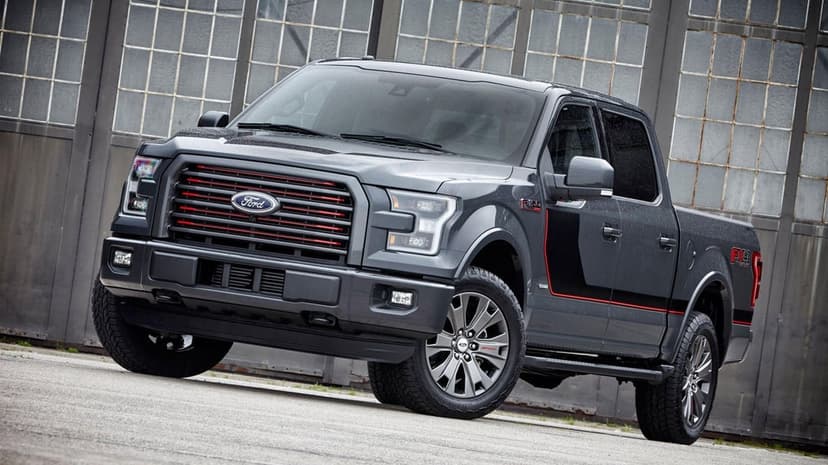Dark gray Ford F-150 truck with red accents parked in front of an industrial window wall on wet pavement.