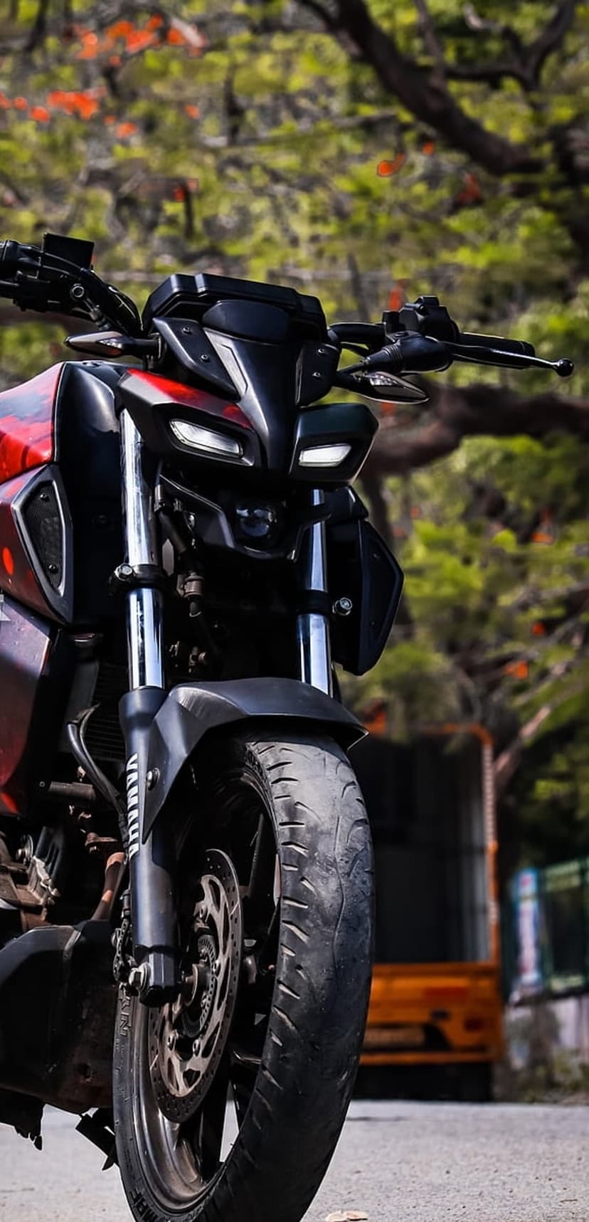 Yamaha MT motorcycle with red accents and dual headlights parked on a paved road with a blurred forest backdrop.
