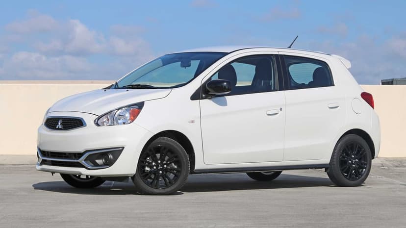 White Mitsubishi Mirage hatchback with black wheels parked on a gray concrete rooftop under a bright blue sky.