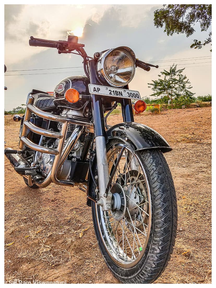 Royal Enfield motorcycle with chrome engine and spoked wheels parked on a gravel path during a golden sunset.