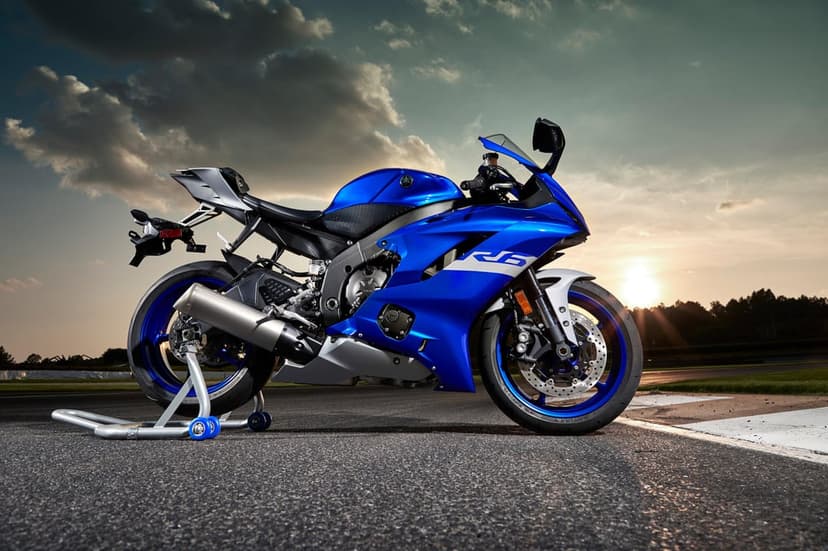 Blue Yamaha R6 sportbike on a paddock stand at a racetrack with a dramatic sunset and cloudy sky background.