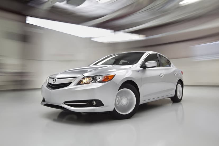 Silver Acura ILX Hybrid sedan at a three-quarter angle with motion-blurred wheels in a bright studio background.