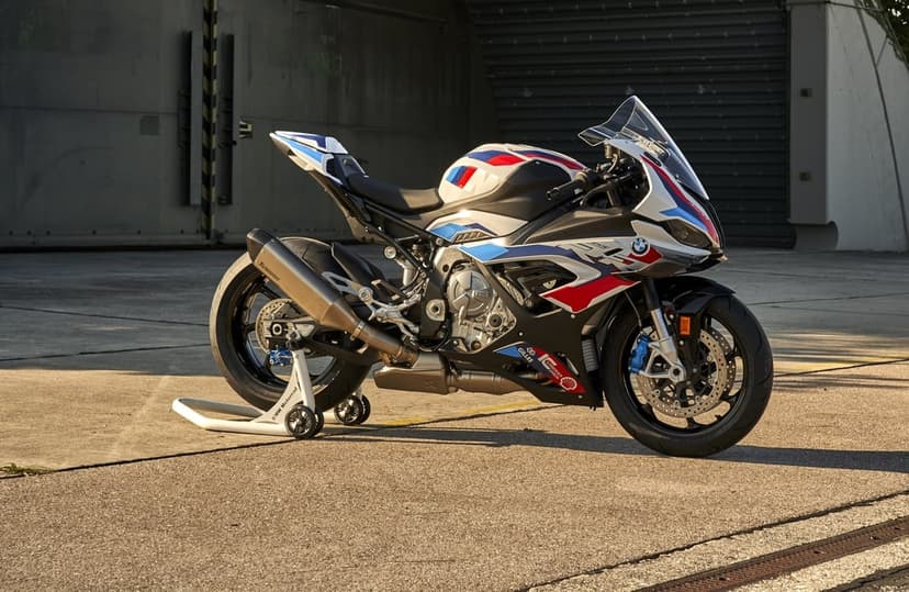 BMW M 1000 RR sport motorcycle in white, red, and blue livery on an airfield with golden sunset lighting.