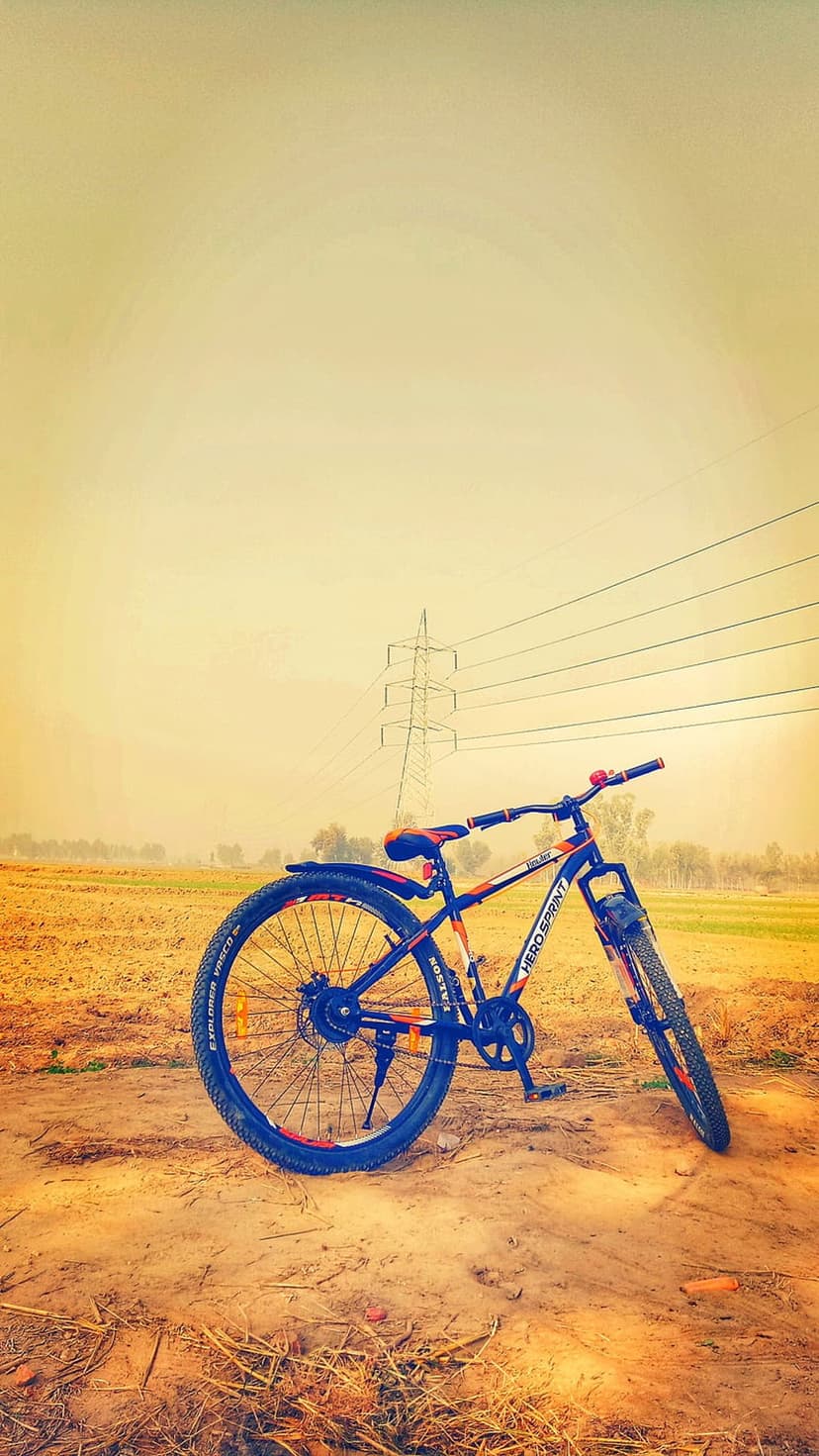 Blue and orange bicycle parked on a dry dirt path under high-voltage power lines against a hazy yellow sky.