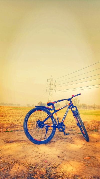 A bicycle rests in a dusty field under power lines.