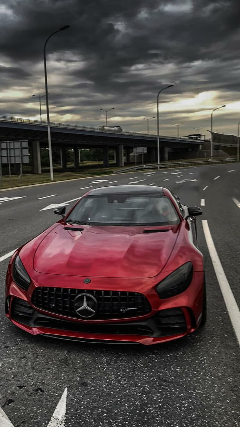 Red Mercedes-AMG GT Coupe with an aggressive grille parked on an asphalt highway under a dark, cloudy sky.