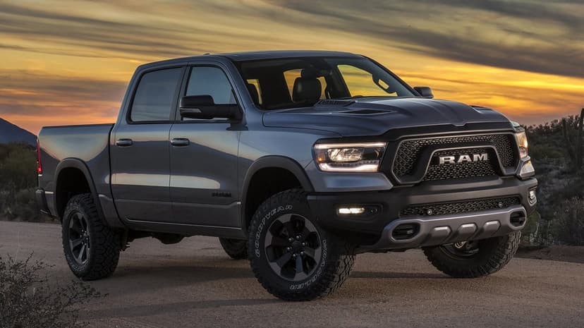 Gray Ram 1500 Rebel truck on a dirt road at sunset with glowing headlights and a colorful sky.
