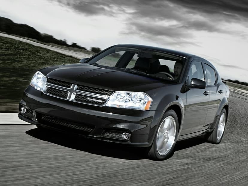 Black Dodge Avenger sedan driving fast on an asphalt road under a dramatic overcast sky with motion blur.