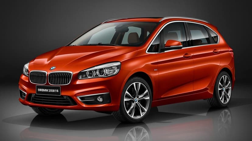 Orange BMW 2 Series Active Tourer in a studio with metallic paint reflections and a dark gray background.
