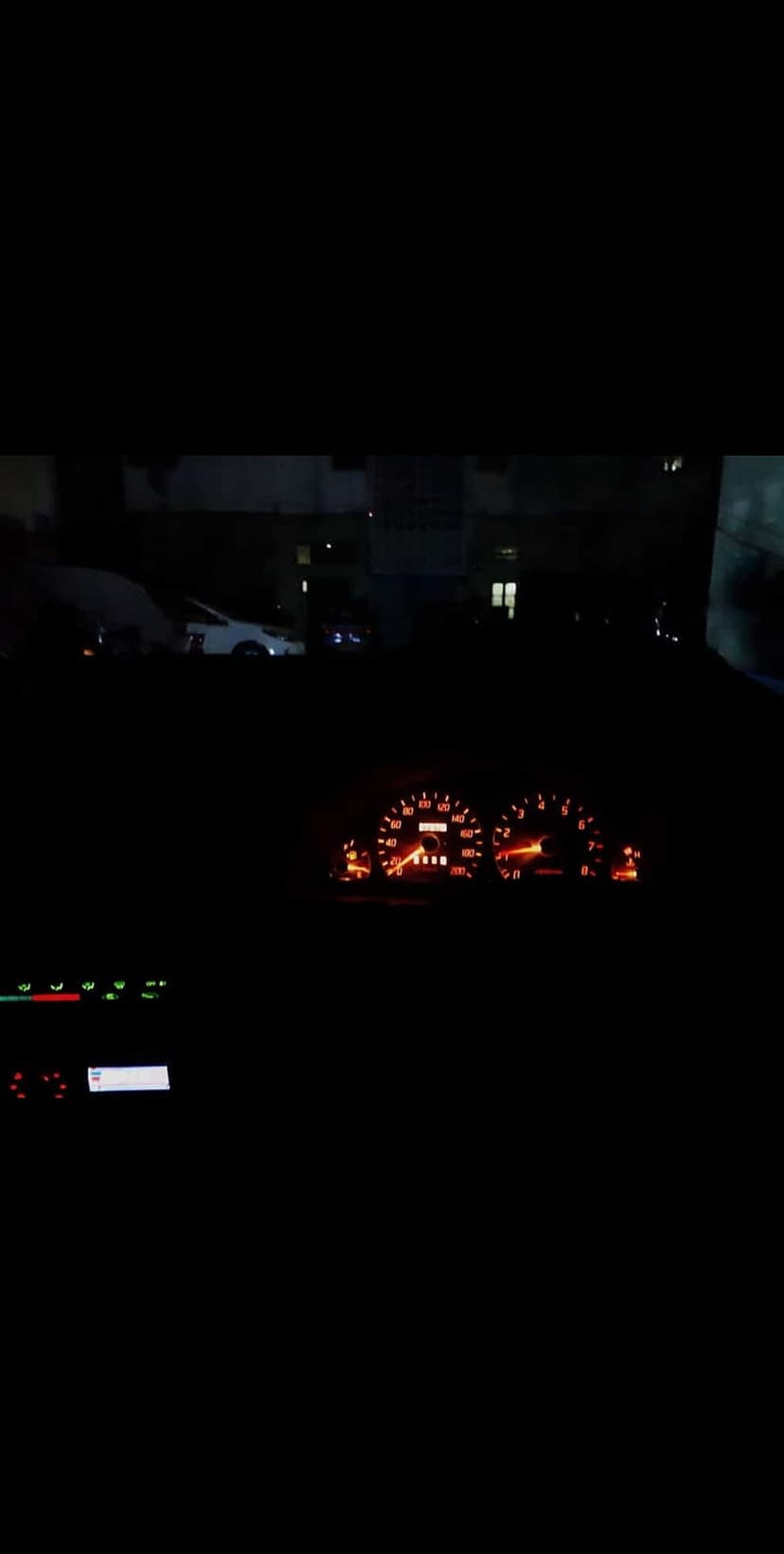 Amber-lit analog speedometer and tachometer needles glow within a dark car dashboard during a night drive.