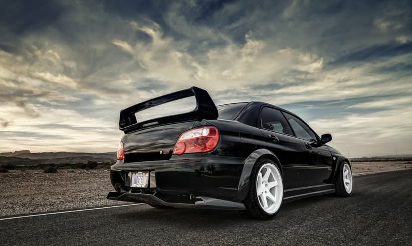 Modified black Subaru WRX STI with white wheels and widebody kit on a desert road under a cloudy sky.