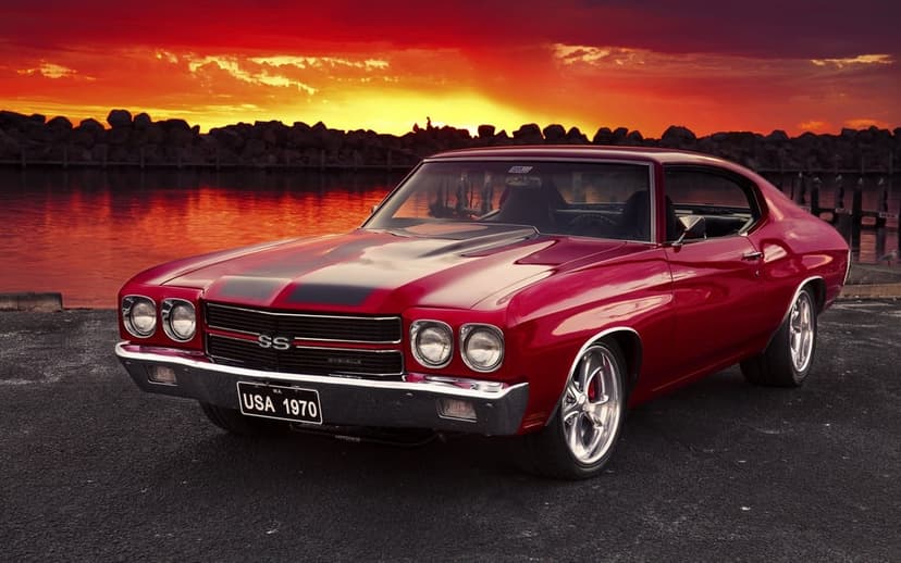 Red 1970 Chevrolet Chevelle SS with black stripes parked on a pier during a fiery orange and red sunset landscape.