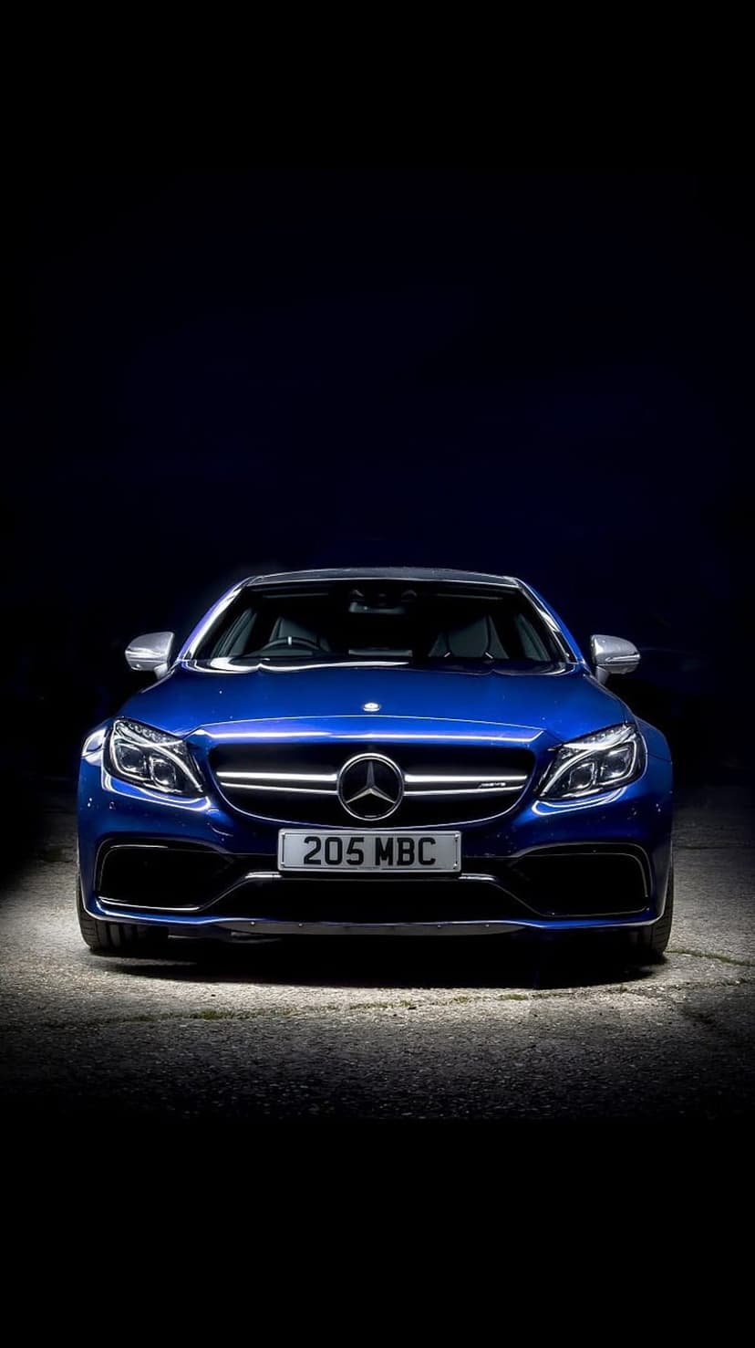 Mercedes-AMG C63 S Coupe in blue shows its front grille and headlights against a dark, dramatic background.