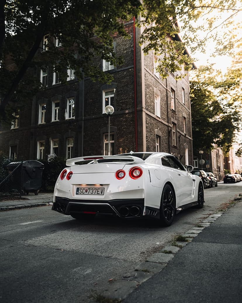 Nissan GT-R rear view on a cobblestone street with sunlight filtering through trees near a brick building.