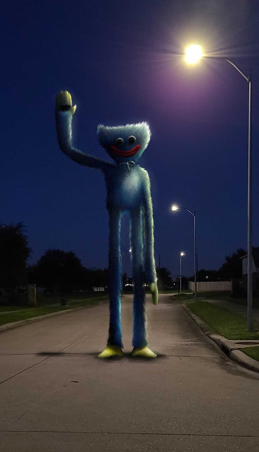 Tall blue furry creature with long legs and a wide red smile waving on a dark suburban street at night.
