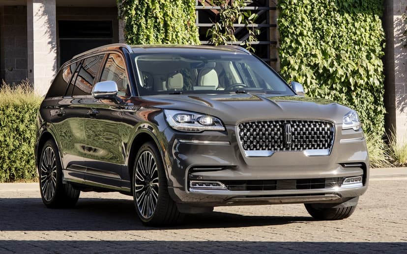 Grey Lincoln Aviator SUV parked on a stone driveway in front of a modern building with green vines.