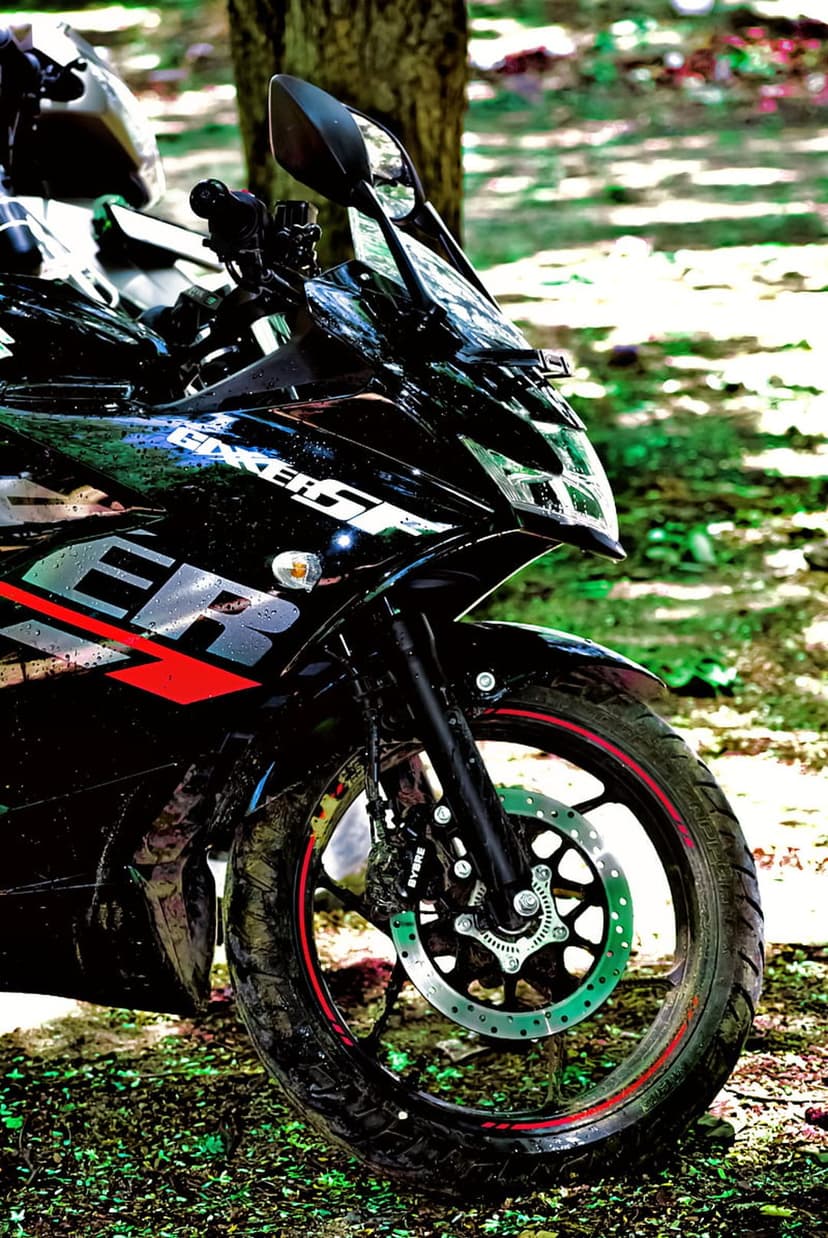 Black Suzuki Gixxer SF motorcycle front wheel and fairing branding detail parked in a sunny forest setting.