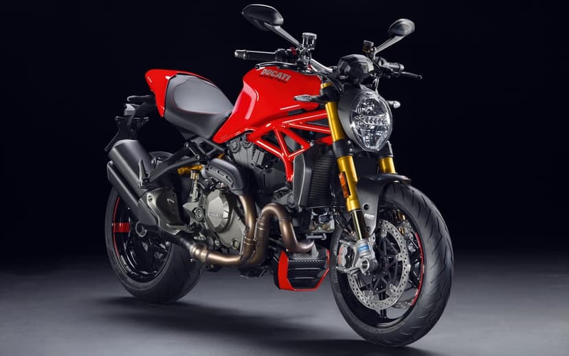 Red Ducati Monster sportbike with gold forks and black trellis frame parked against a dark studio backdrop.