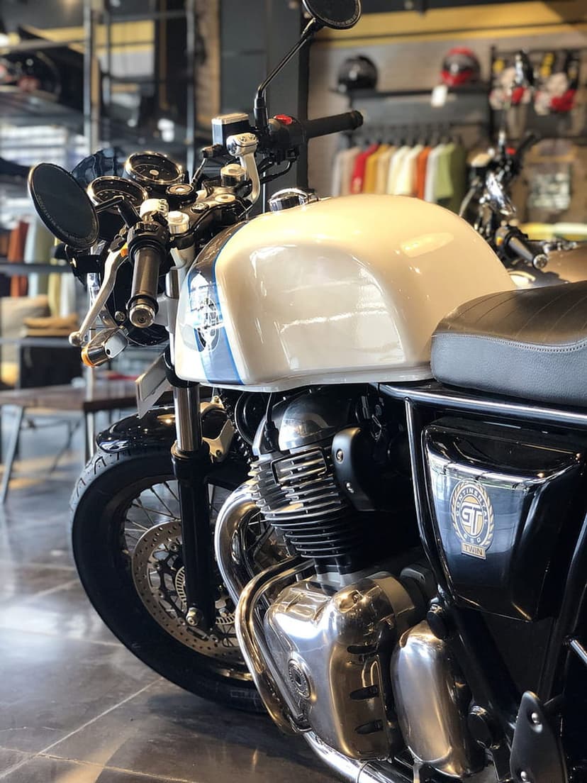 Royal Enfield fuel tank in white and blue rests above a chrome engine within a soft-lit motorcycle showroom.