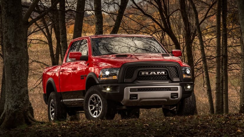 Red Ram 1500 Rebel truck parked in a forest with autumn leaves, featuring a black grille and silver bumper.