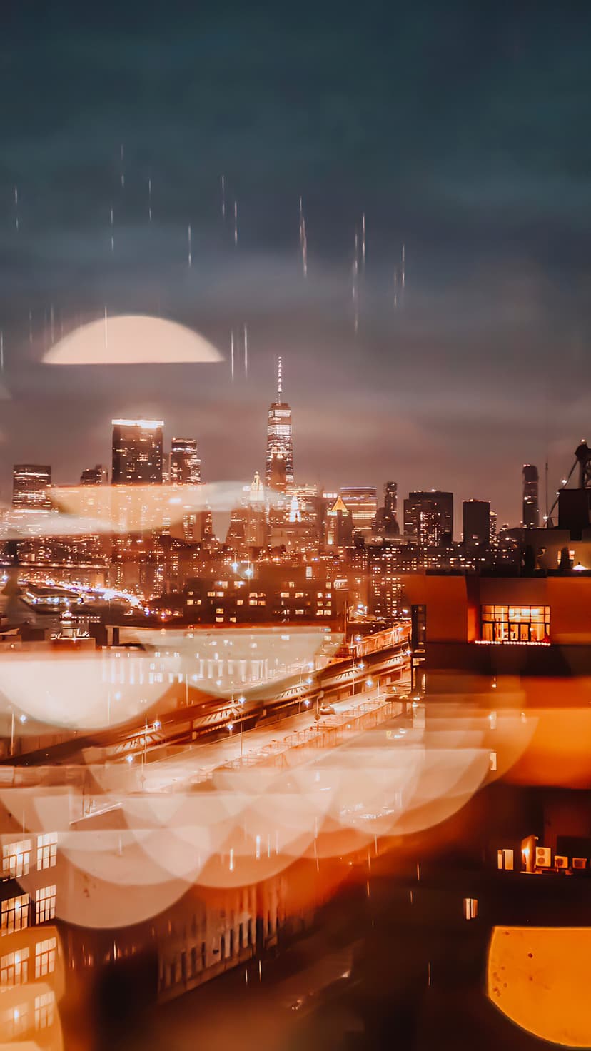 One World Trade Center stands behind a rain-slicked window with glowing golden bokeh and blue city lights.