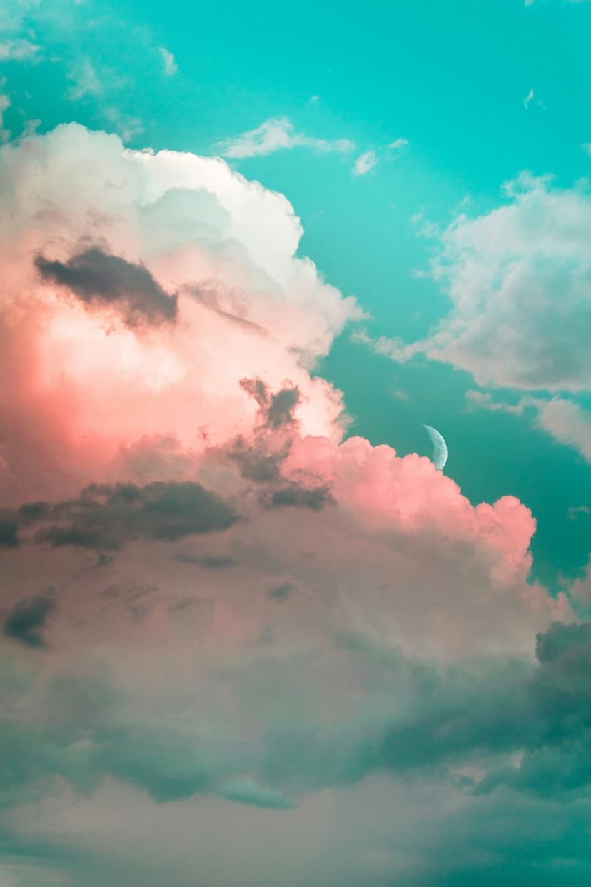 Billowing pink and teal clouds surround a glowing silver crescent moon in a deep twilight sky during dusk.