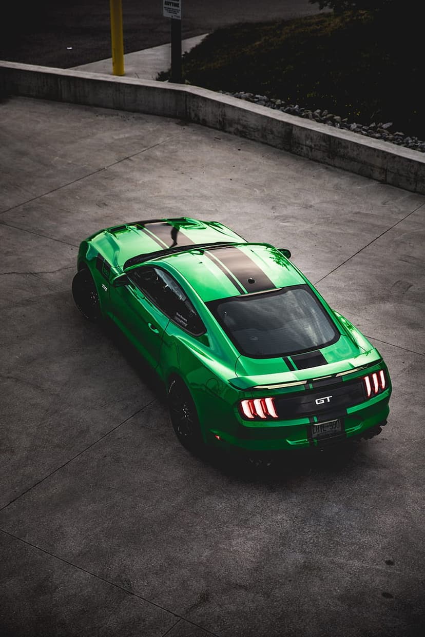 Lime green Ford Mustang GT with black racing stripes and lit taillights parked on a gray concrete surface.