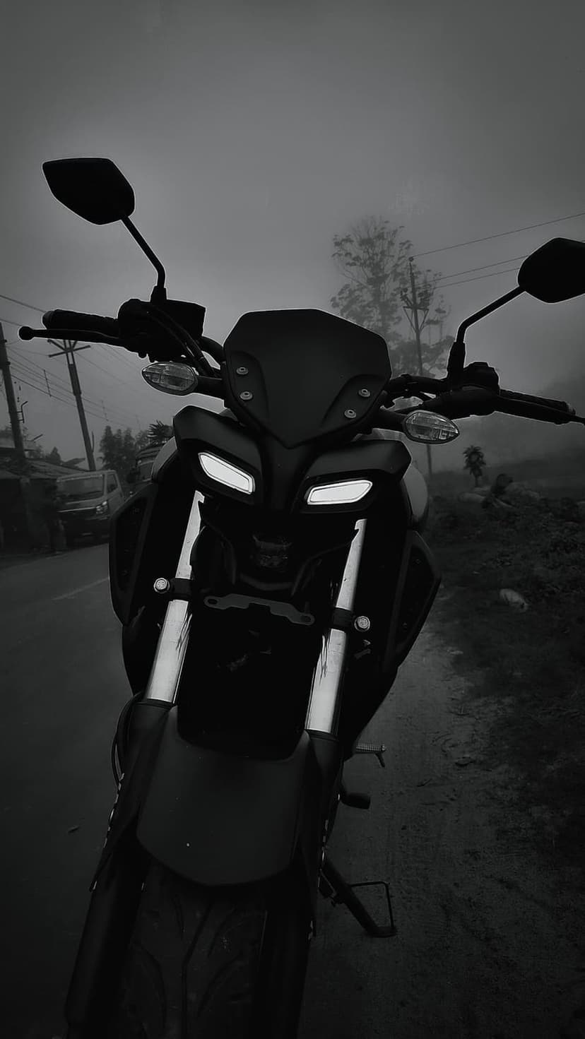 Yamaha MT motorcycle with glowing LED headlights stands on a wet asphalt road amidst thick morning fog and trees.