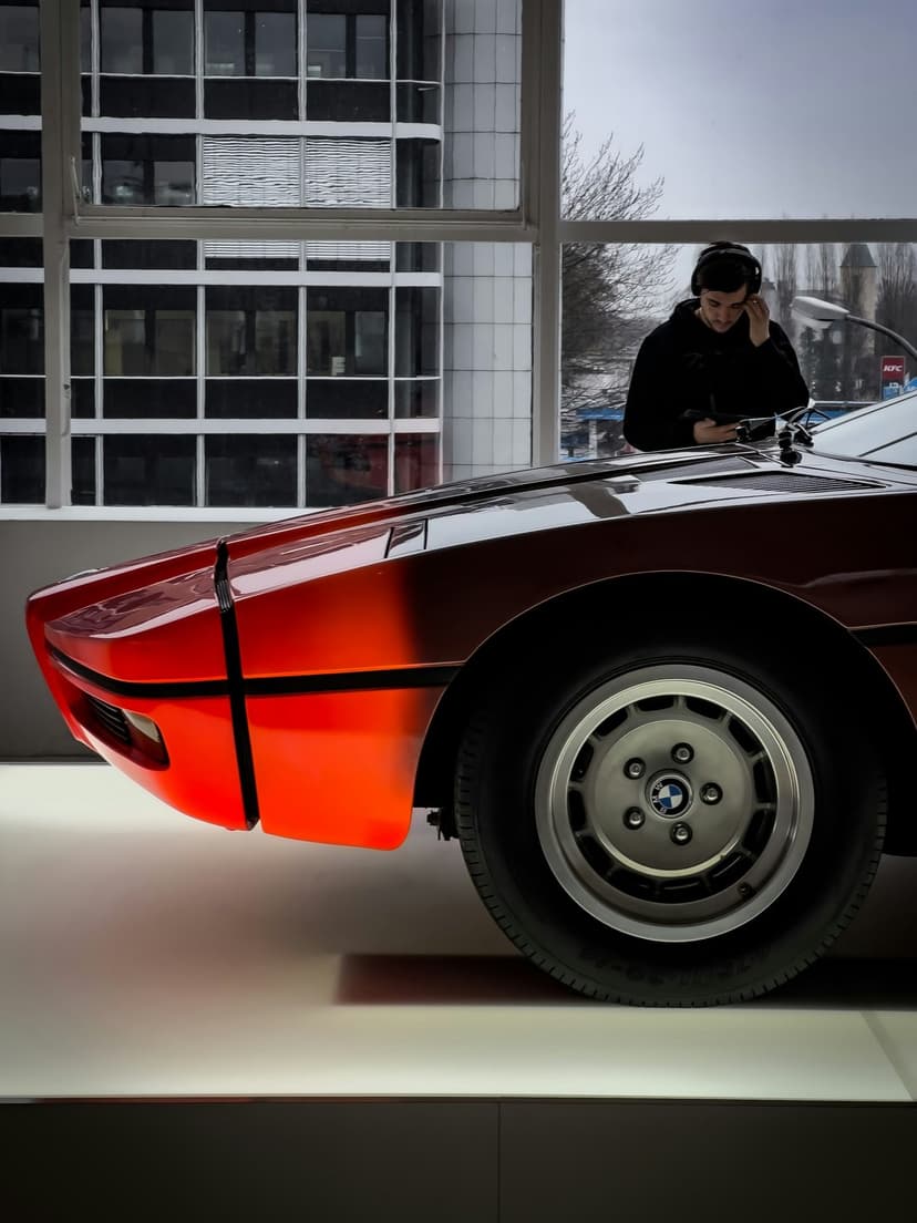 Red BMW M1 vintage sports car front profile with silver wheels inside a modern architectural showroom.