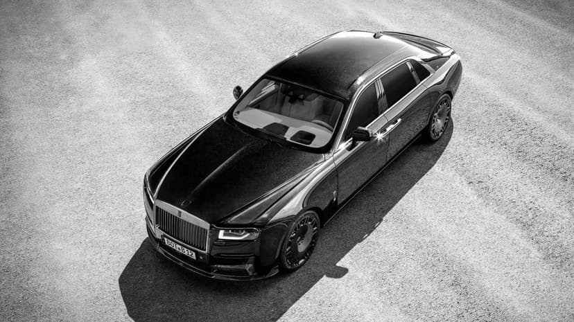 Black modified luxury sedan viewed from above on a textured gray asphalt surface in monochrome.
