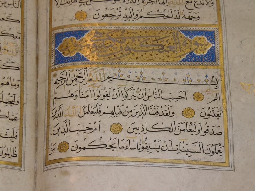 Arabic calligraphy on a Quran page with gold leaf illumination and blue decorative borders on parchment.