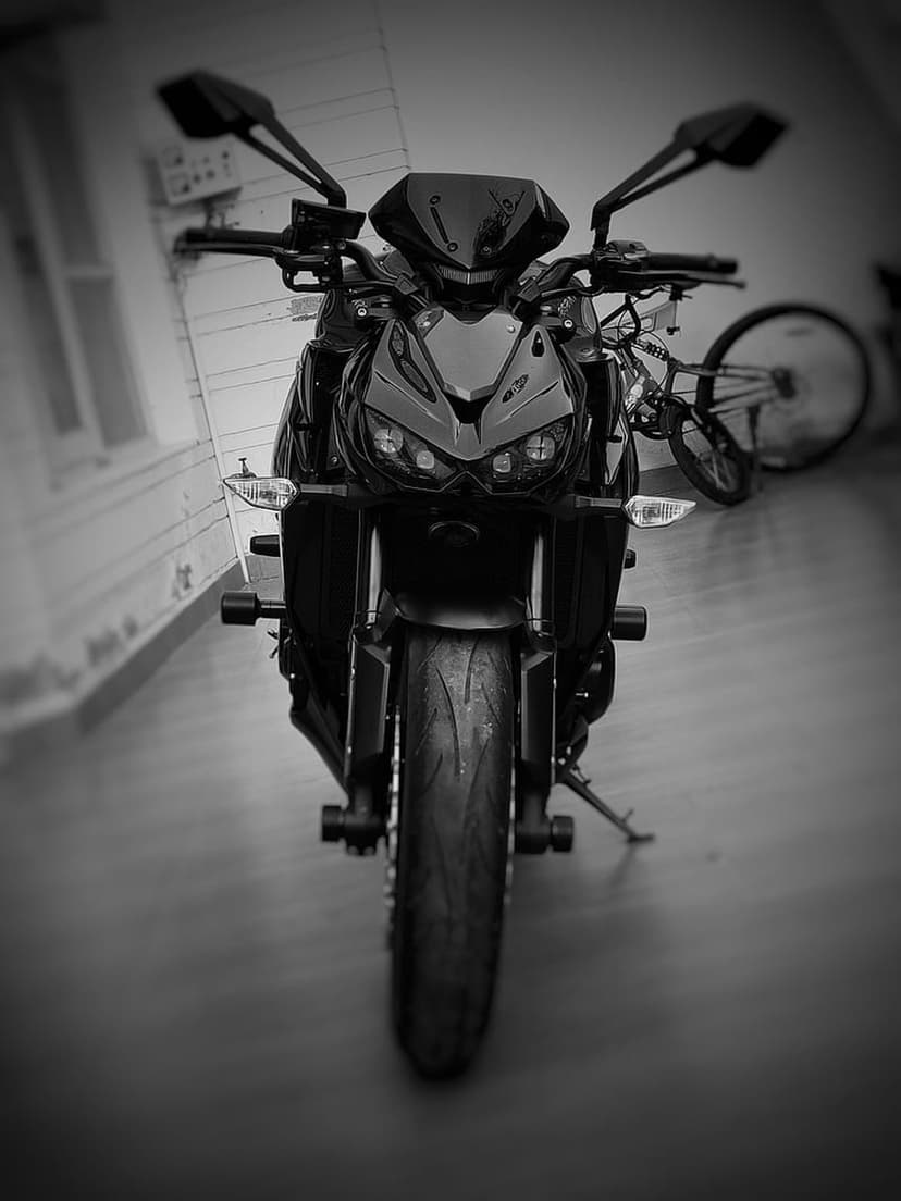Black motorcycle front view with dual headlights and sleek windshield against a blurred bicycle background.